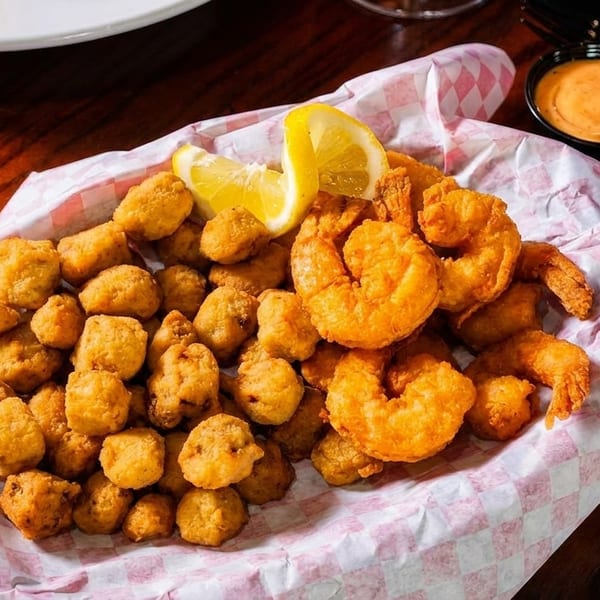 Basket of crispy fried shrimp and hush puppies with lemon wedges and dipping sauce.