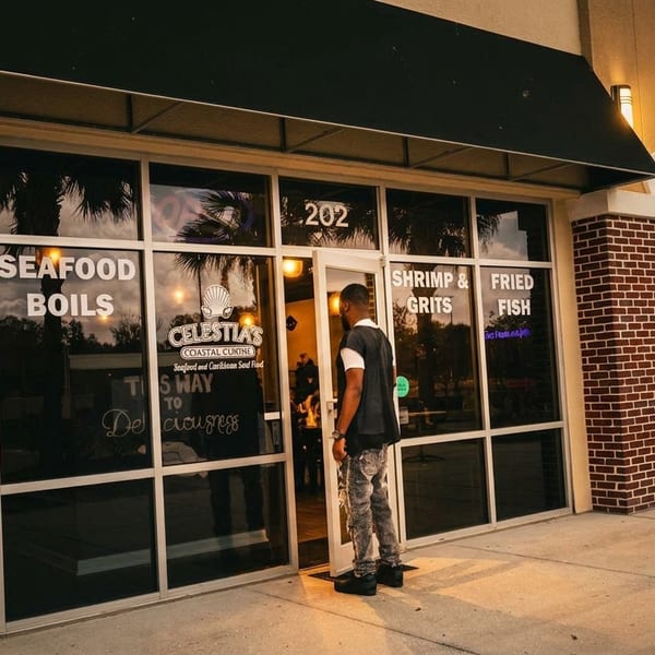 A man stands at the entrance of Celestia's Coastal Cuisine restaurant, with menu items visible on the windows.